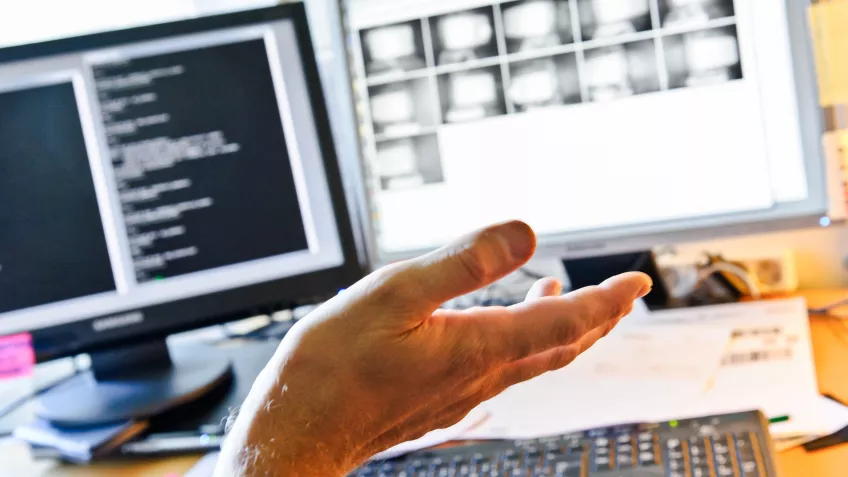 An open hand is in front of two computer screens. Photo.