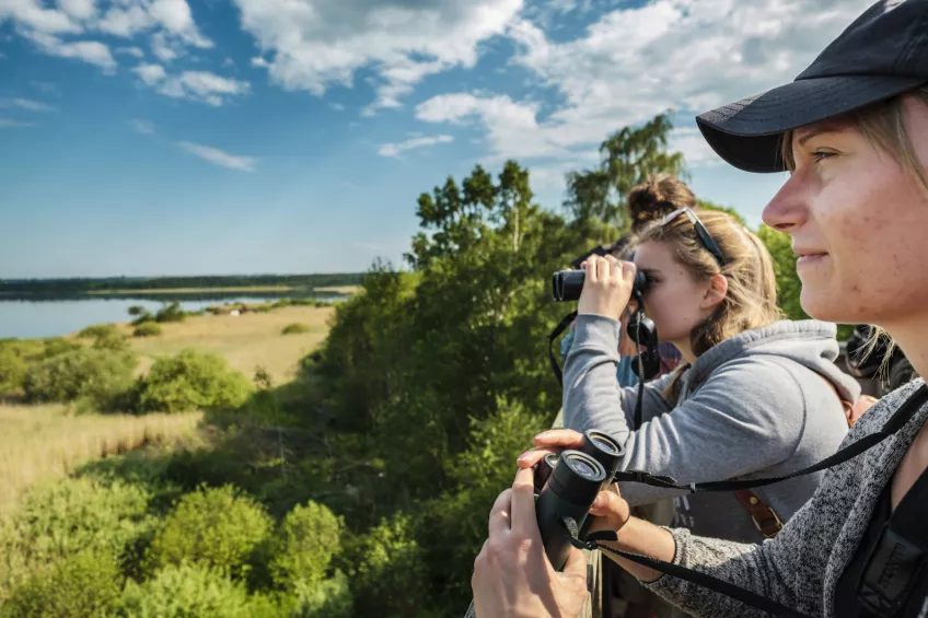 Two people sitting with binoculars. Photo.